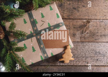 Weihnachtsgeschenk-Kontext mit einem Geschenk in braunem Papier mit winzigen Tannen mit ungeschriebenem Tag und einem Weihnachtskeks auf einem rustikalen Tisch Stockfoto