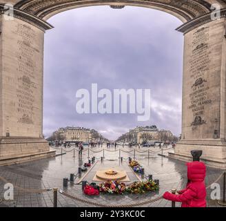 Blick von unter dem Triumphbogen, über die Ewige Flamme, das Denkmal für den unbekannten Soldaten und Champs-Elysees Boulevard, auf einer düsteren, regnerischen Straße Stockfoto