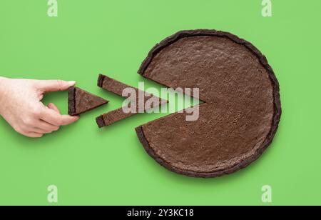 Blick über dem Kopf mit der Hand einer Frau, die ein winziges Stück Schokoladentorte nimmt, minimalistisch auf grünem Hintergrund Stockfoto