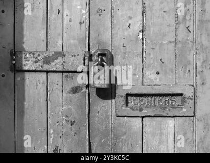 Nahaufnahme einer alten Holztür mit gerissener verblasster Farbe und einem rostigen geschlossenen Vorhängeschloss und einem alten Metallbriefkasten Stockfoto