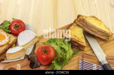 Köstliches Essen auf einem Holztisch, französische Sandwiches genannt Croque Madame und Croque Monsieur, Tomaten, Weißkäse und Salat Stockfoto