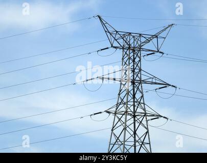 Ein hoher elektrischer Pylon aus Metall mit mehreren Kabeln gegen einen blauen, bewölkten Himmel Stockfoto