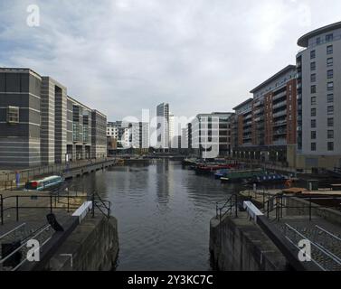 Ein Blick auf das Dock von leeds von den Schleusentoren zeigt Gebäude am Wasser, Büros und Wohngebäude mit Hausbooten, die im Wasser vertäut sind Stockfoto