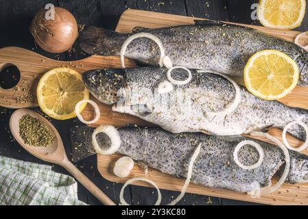 Close-up mit frischen Forelle, bestreut mit Kräutern, Gewürzen, Zwiebelringen und Zitronenscheiben, auf einem hölzernen Schneidebrett, auf einem Vintage-Tisch Stockfoto