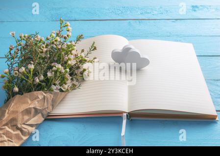 Zwei hölzerne Herzen auf leeren Notizbuchseiten und weißer Blumenstrauß in Vintage-Papier, auf einem blauen Holztisch. Valentinstag-Geschenk. Frauen-Tagesrahmen Stockfoto