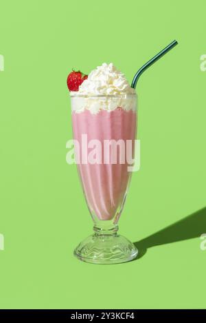 Milchshake mit Erdbeergeschmack in hellem Licht, minimalistisch auf einem grünen Tisch. Köstlicher hausgemachter Milchshake mit Vanilleeis und Erdbeeren Stockfoto