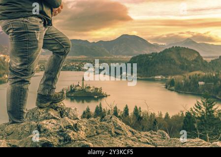 Bild mit den Beinen eines Mannes, touristische kletterte auf den Felsen oberhalb der See Bled in Slowenien, Blick auf den wunderschönen Sonnenaufgang und die Julischen Alpen Stockfoto