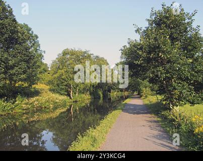 Ein langer gerader Pfad entlang eines Kanals im Sommer mit Bäumen, die sich im hellen Sommersonnenlicht in der Nähe von luddenden in West yorkshire spiegeln Stockfoto