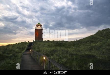 Sonnenuntergangslandschaft auf Sylt Island in der Nordsee, Deutschland. Wunderschöne Landschaft mit rotem Backsteinleuchtturm auf einem Hügel unter einem wolkigen Himmel Stockfoto