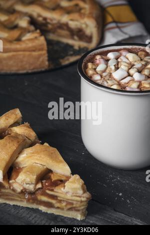 Tasse heiße Schokolade mit Mini-Marshmallows und einem Stück Apfelkuchen auf einem rustikalen Tisch. Traditionelle amerikanische Desserts. Frühstückstisch. Hausgemacht Stockfoto