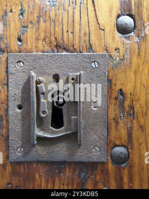 Ein großes quadratisches rostiges Eisenschloss mit Schlüsselloch in einer alten lackierten Holztür mit sichtbarem Ende des Schlüssels und Metallnieten Stockfoto