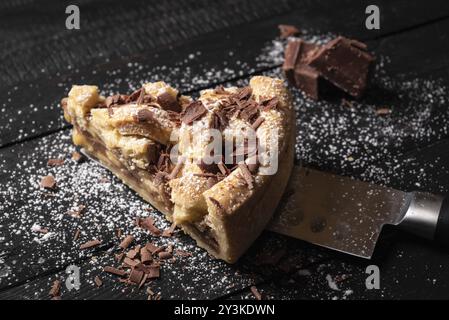 Nahaufnahme eines Stücks Apfelkuchen auf einem Messer, verziert mit Puderzucker und Schokolade, auf einem schwarzen Tisch. Hausgemachte köstliche süße Torte Stockfoto