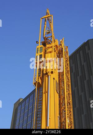 Ein gefalteter gelber Baukran mit seitlich umreiftem Portal, der darauf wartet, auf einer städtischen Baustelle eingesetzt zu werden Stockfoto