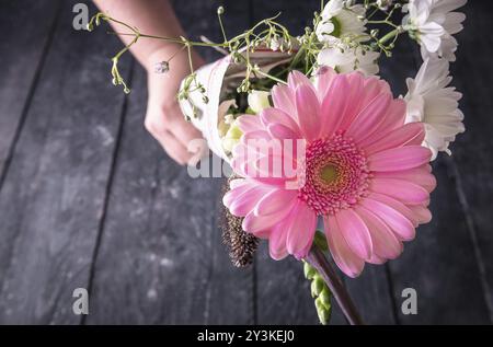 Romantisches Themenbild mit einem schönen Blumenstrauß aus Chrysanthemen, in Zeitung gewickelt, in der Hand gehalten und auf einem Vintage-Wald auf die Kamera gerichtet Stockfoto