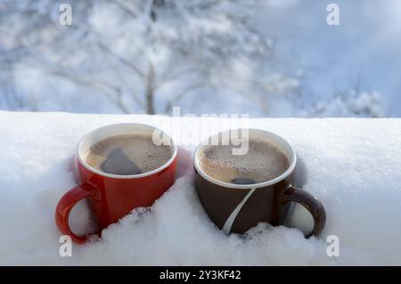 Dampfender heißer Kaffee in zwei Tassen, im Schnee vergraben, auf einem Balkon, an einem hellen Wintermorgen. Frühstück für zwei Personen. Gemütliches Winterkonzept Stockfoto