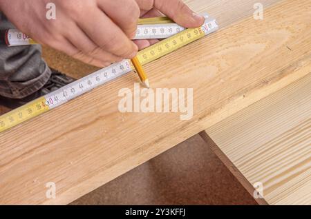 Nahaufnahme mit den Händen eines Mannes, der ein Maßband gegen ein Holzbrett hält und mit einem Bleistift eine Markierung macht Stockfoto