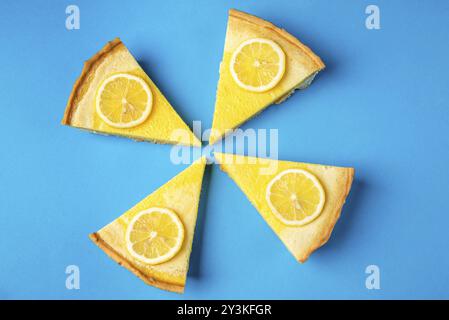 Vier Stücke Zitronentorte auf blauem Hintergrund, verziert mit gelben Zitronenscheiben. Selbstgebackenes Gebäck. Süß-saures Dessert. Zitruskuchen Stockfoto