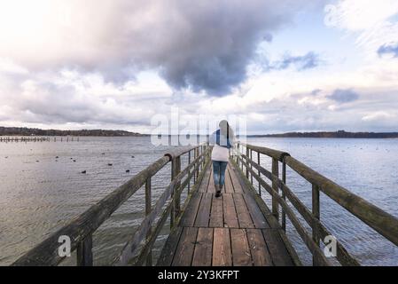 Junge Frau, die allein auf einer rustikalen Holzbrücke über den Chiemsee, auch Bayerisches Meer genannt, in der Nähe von Rosenheim, Deutschland, Europa, spaziert Stockfoto