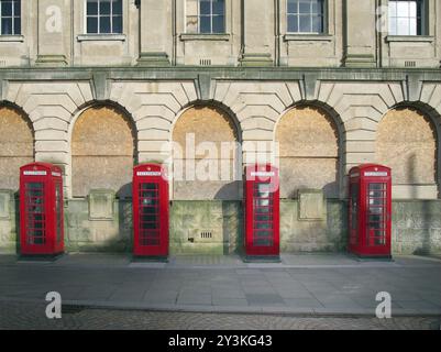 Eine Reihe von vier traditionellen britischen roten Telefonzellen vor einem alten verlassenen Postgebäude in blackpool, england Stockfoto