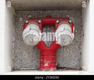 Nahaufnahme eines roten doppelten, in die Gebäudewand eingelassenen Außenhydranten Stockfoto