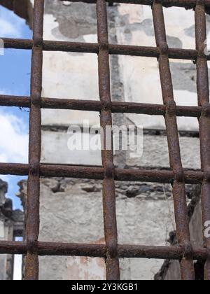 Eine Nahaufnahme eines rostenden Eisenzauns mit Gittern vor einem zerstörten Gebäude Stockfoto