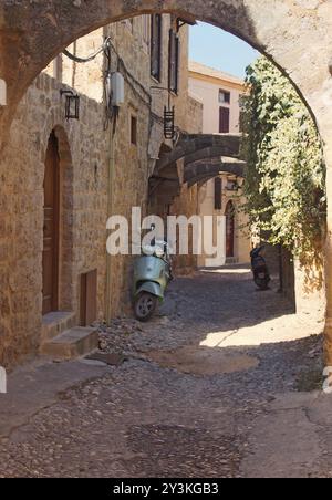 Eine typische ruhige Kopfsteinpflasterstraße in rhodos Stadt mit alten gelb bemalten Häusern und einem Steinbogen mit sonnendurchflutetem Sommerhimmel Stockfoto