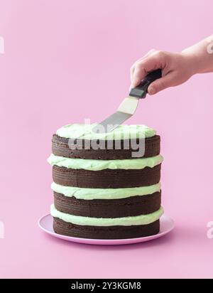 Die Frau macht einen Minzschokoladenkuchen, minimalistisch auf pinkfarbenem Hintergrund. Köstlicher hausgemachter Kuchen mit dunkler Schokolade und Buttercreme mit Minzgeschmack Stockfoto