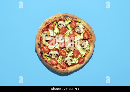 Blick von oben mit einer hausgemachten Pizza Minimalist auf einem blauen Tisch. Köstliche vegane Pizza mit Zucchini, Tomaten und Pilzen Stockfoto