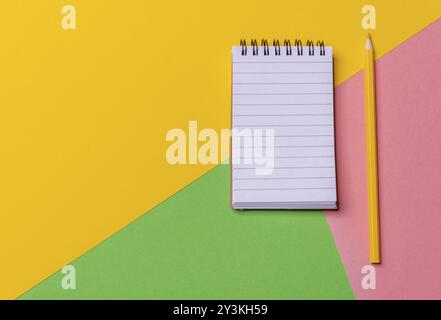Über dem Schreibtisch in drei Farben mit leerem Spiralnotizbuch und gelbem Bleistift. Notizen machen. Zurück zur Schule. Bildungskonzept Stockfoto