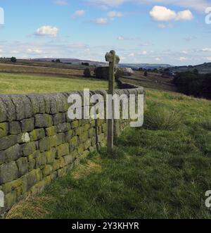 Offene Landschaft mit Wegweiser neben einer Trockenmauer mit grünen Feldern und Mooland in der Ferne in yorkshire england Stockfoto