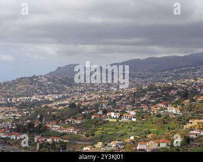 Blick aus der Vogelperspektive auf den Stadtrand von funchal auf Madeira mit Bauernhöfen und Häusern mit Bergen und bewölktem Himmel in der Ferne Stockfoto