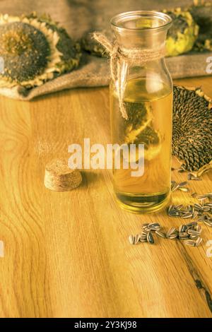 Flasche mit kalt gepresstem Öl auf einem Holztisch mit Sonnenblume Pflanzen und Samen alle über sie Stockfoto