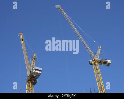 Zwei große gelbe Turmkräne arbeiten auf einer Baustelle vor blauem Himmel Stockfoto