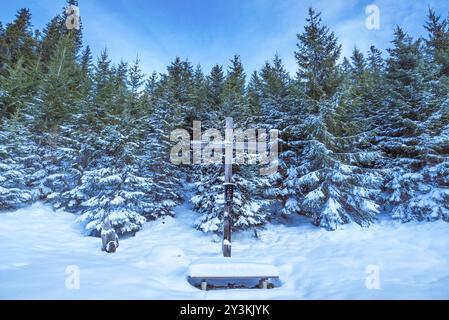 Winterszene mit einem alten Holzkreuz und einem Tannenwald, bedeckt mit Schnee, unter einem blauen Himmel. Aufnahme in Ehrwald, Österreich, Europa Stockfoto