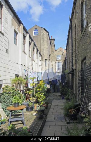 Eine Gasse zwischen den Straßen mit Reihen traditioneller Steinhäuser in hebden Bridge West yorkshire mit Waschtrocknung an den Linien und Topfpflanzen in hellen Töpfen Stockfoto