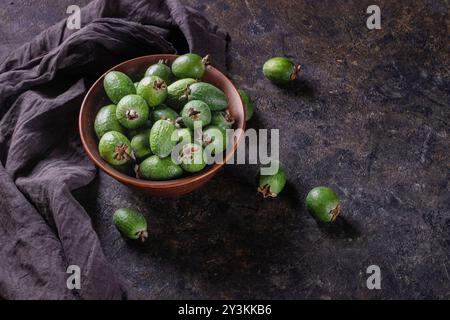 Tropische Früchte grüne reife Feijoa sellowiana Beeren in einer Tonschale und auf einem Tisch auf dunklem Hintergrund mit Kopierraum für Text Stockfoto