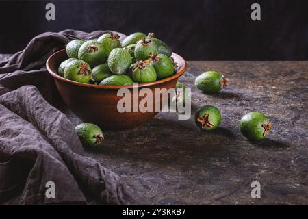 Tropische Früchte grüne reife Feijoa sellowiana Beeren in einer Tonschale und auf einem Tisch auf dunklem Hintergrund mit Kopierraum für Text Stockfoto