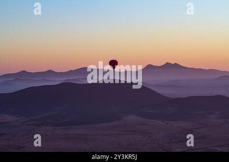 Ein einsamer Heißluftballon erwacht zum Zauber der Dämmerung und gleitet anmutig über die ruhige Wüstenlandschaft Stockfoto