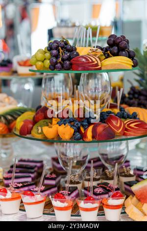 Exquisites Arrangement aus frisch geschnittenem Obst und eleganten Desserts auf einer mehrstufigen Ausstellung. Stockfoto