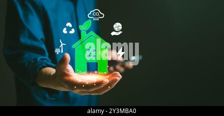 Grünes Smart Home-Hologramm in der Hand, umgeben von umweltfreundlichen Symbolen. Förderung von Nachhaltigkeit und erneuerbaren Energien. Ideal für Umweltkampagnen, Stockfoto