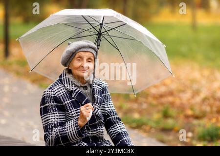 Ältere Frau im grauen Mantel mit Regenschirm im Herbst Stockfoto