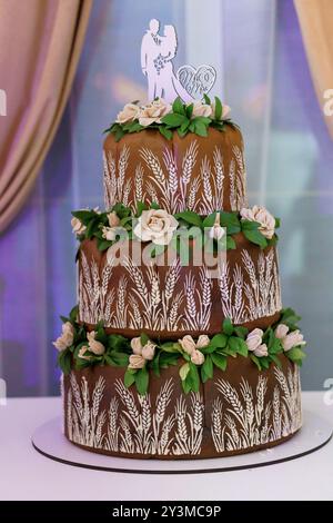 Eleganter dreistöckiger Hochzeitstorte mit Schokoladenmotiven und Blumendekorationen. Stockfoto