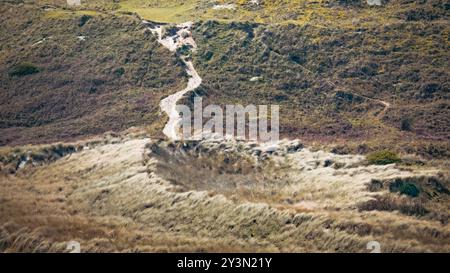 Ein gewundener Schotterweg durch grasbewachsene Hügel an einem sonnigen Tag in einer ruhigen ländlichen Landschaft. Stockfoto
