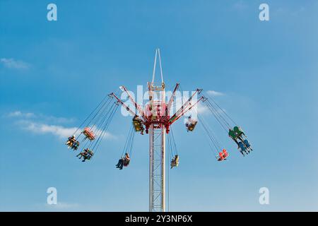 Eine farbenfrohe Schaukelfahrt in einem Vergnügungspark mit mehreren Sitzplätzen, die an einem zentralen Turm hängen. Fahrer genießen das Erlebnis gegen eine Clea Stockfoto