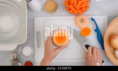 Rezept für Butternusskürbis-Suppe, Zubereitungsprozess. Rohes Gemüse und Gewürze in Nahaufnahme auf dem Küchentisch, flacher Lay. Frauenhände schälen Kürbis, flach Stockfoto
