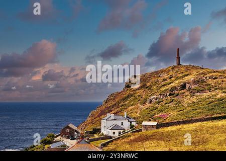 Ein malerischer Blick auf die Küste mit einem weißen Haus und einem historischen Schornstein auf einem Hügel mit Blick auf das Meer. Der Himmel ist teilweise bewölkt mit leuchtender Farbe Stockfoto