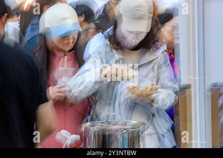 Zwei Frauen mit Mützen genießen bei einem geschäftigen Marktereignis tagsüber Essen von einem Straßenhändler. Verschwommenes Bild. Calgary, Alberta Stockfoto