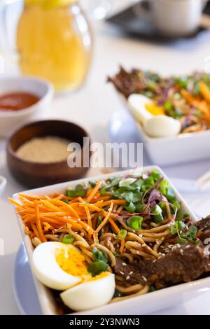 Zu Hause, Nahaufnahme einer köstlichen Ramen-Schüssel mit gekochtem Ei, Gemüse und Rindfleischstreifen Stockfoto