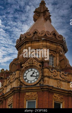 Ein Blick aus der Nähe auf einen historischen Uhrenturm mit komplexen architektonischen Details. Das Zifferblatt zeigt die Zeit an, und der Turm ist mit einem dec Stockfoto
