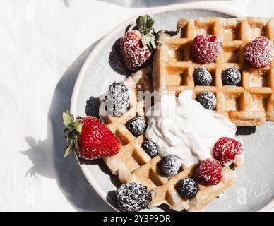 Köstliche goldene Waffeln garniert mit frischen Erdbeeren, Himbeeren, Brombeeren, Heidelbeeren und einem Klecks Schlagsahne, mit Puderpulver bestäubt Stockfoto